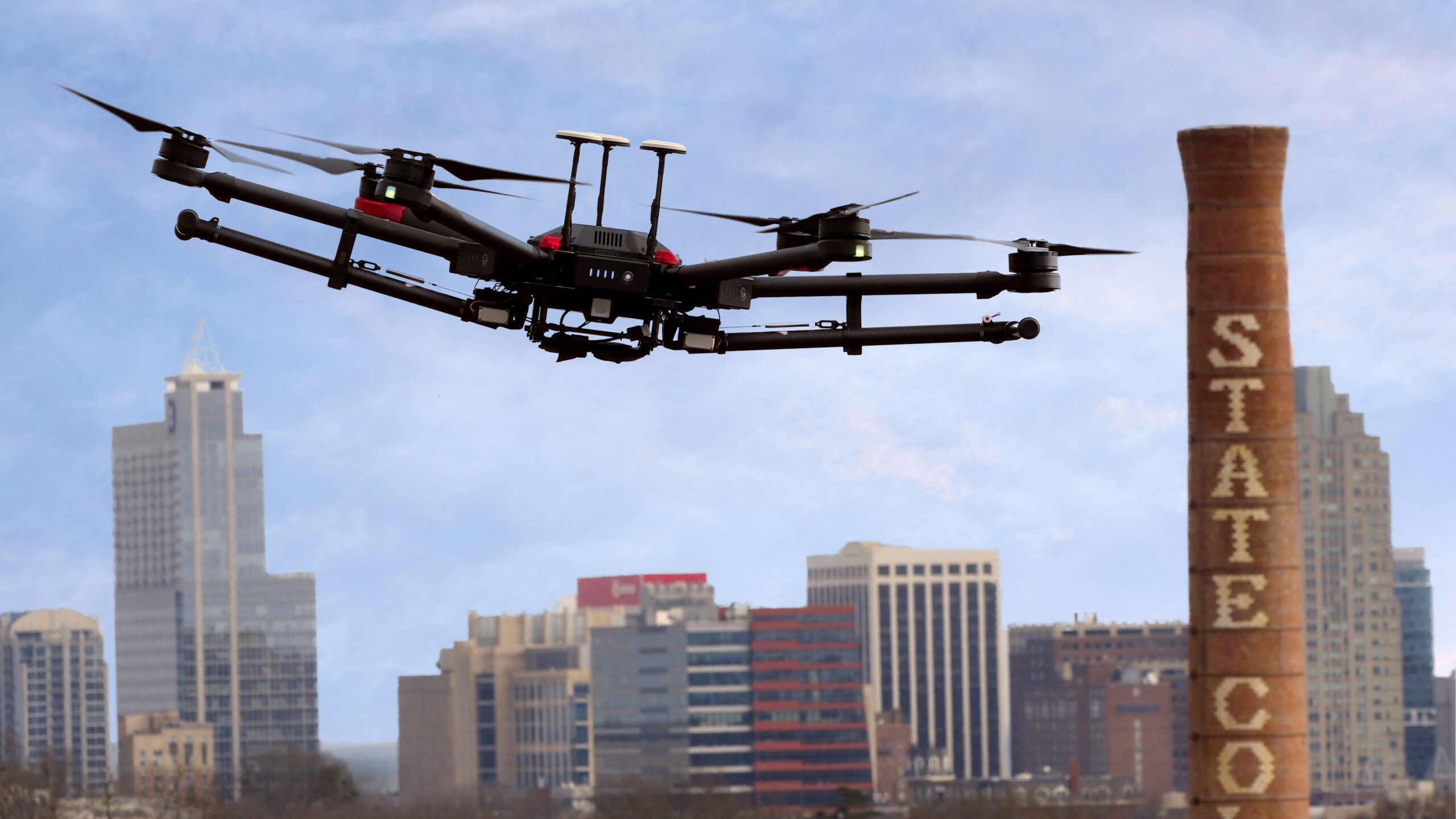 A drone flies over NC State campus with the Raleigh skyline in the background.