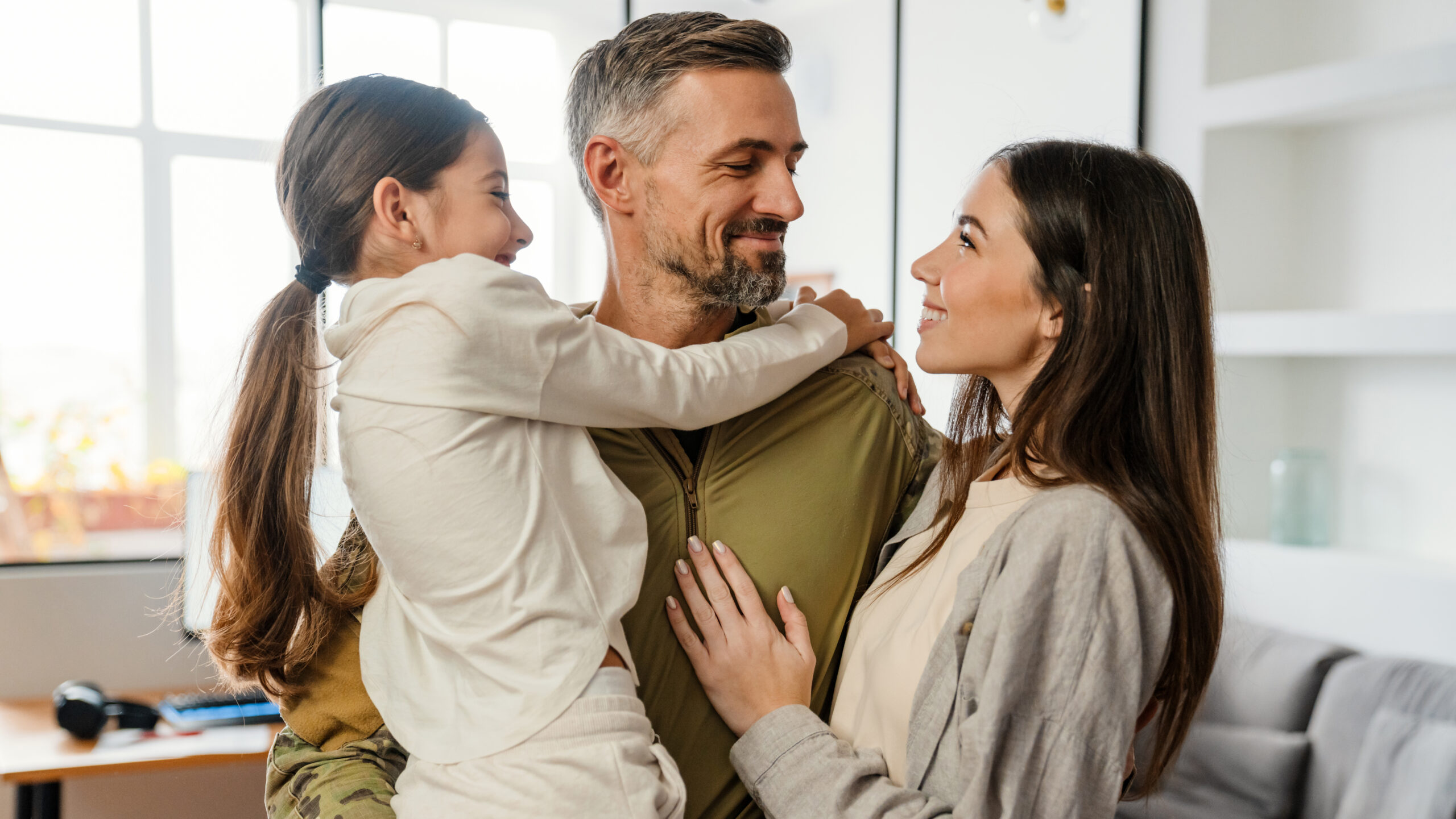 Happy masculine military man smiling and hugging his family indoors
