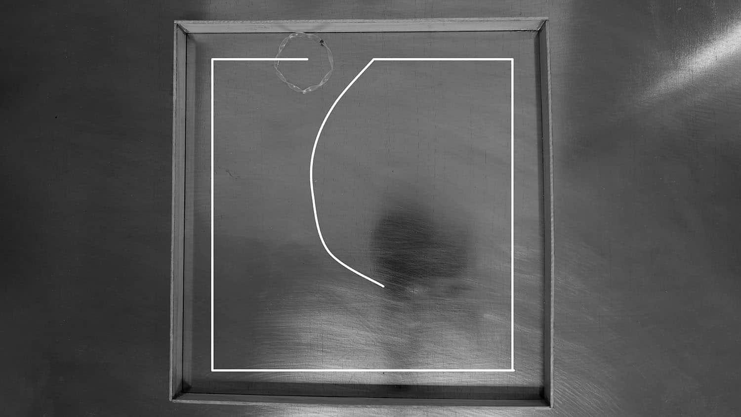 black-and-white video still shows a ringlike object in a square space that has one gap for an entrance. A bright white line shows the path that the object has taken in tracing the contours of the space.