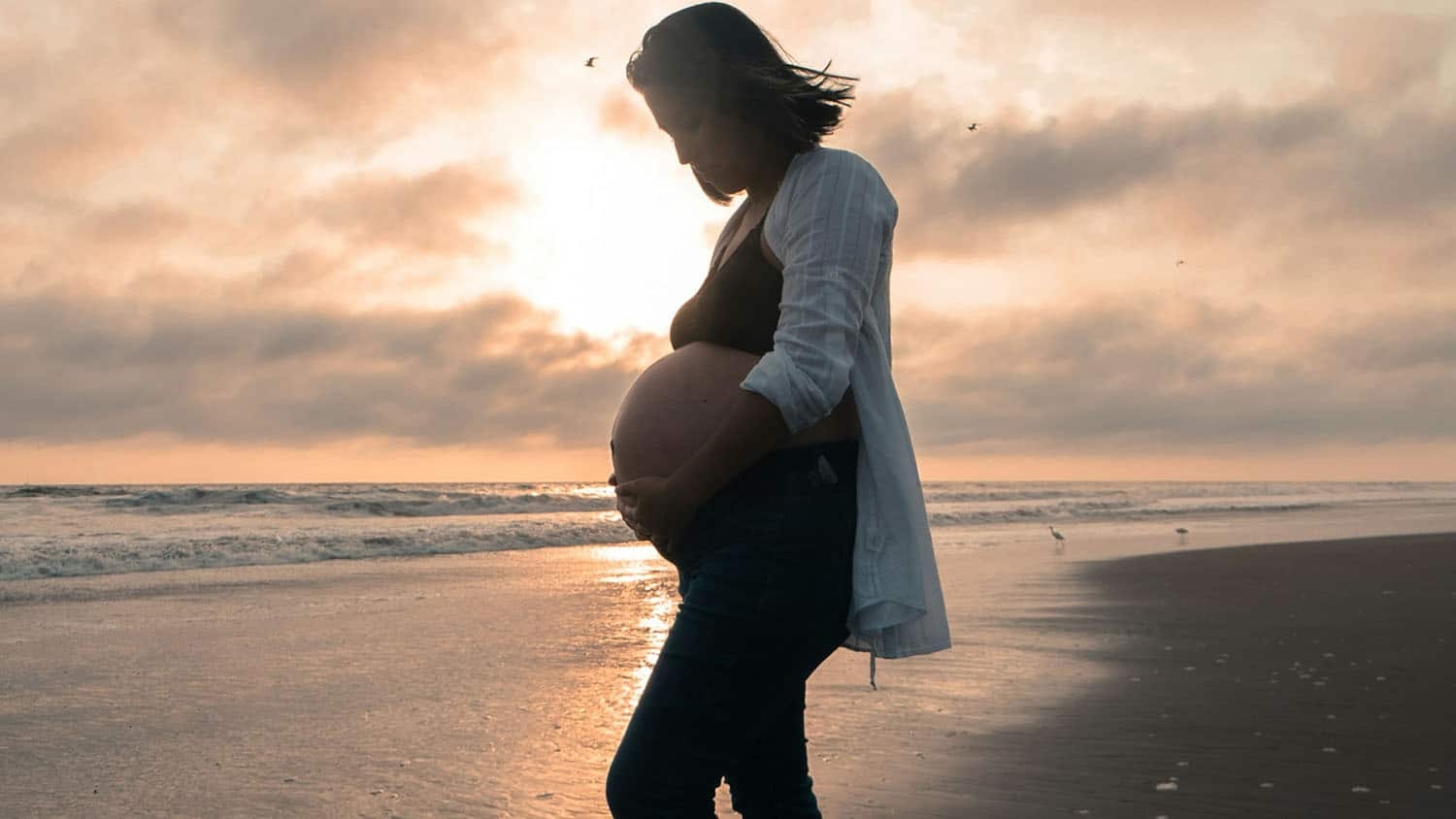 Pregnant women stands on the beach.