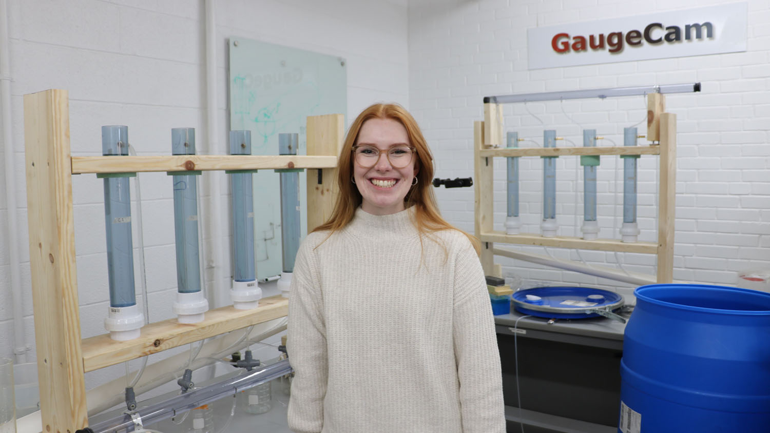 a woman stands next to a series of clear columns in a laboratory