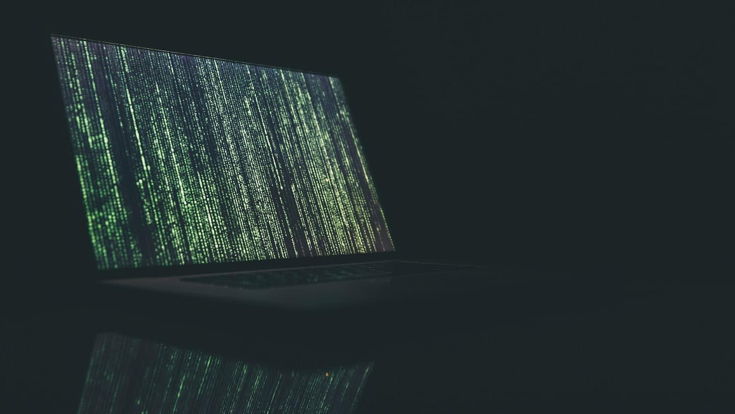 a laptop computer streaming green text sits on a table in a dark room