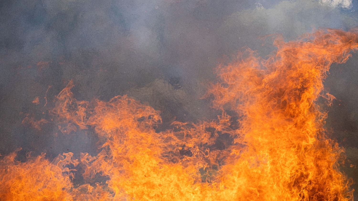 Close-up of bright orange flames and thick gray smoke rising, capturing the intensity of a fire.