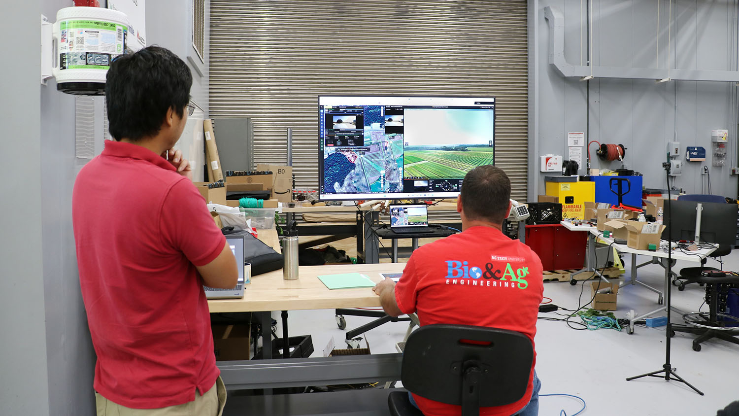 two men inside a building look at a computer screen with a map and live images from a drone