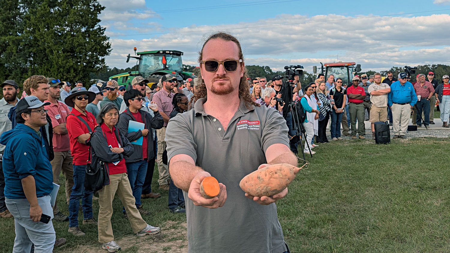 Man holds out cut orange sweetpotato in front of crowd