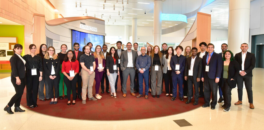 A group of people wearing business casual clothes and lanyards poses for a photo in Hunt Library. 